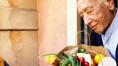 Kadın, Covid 19 salgını sırasında kese kağıdında yemek dağıtıyordu. Verandada alışveriş yapan bir gönüllü var. Engelli yaşlı adamın akıllı telefonu kullanmasına yardım eden gönüllü bir kadın. Yiyecek kutusu bağışı. Sosyal yardım.