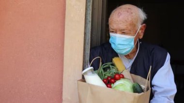 Kadın, Covid 19 salgını sırasında kese kağıdında yemek dağıtıyordu. Verandada alışveriş yapan bir gönüllü var. Engelli yaşlı adamın akıllı telefonu kullanmasına yardım eden gönüllü bir kadın. Yiyecek kutusu bağışı. Sosyal yardım.