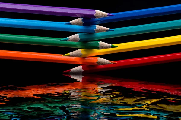 Colored pencils on black background reflected in water. — Stock Photo, Image