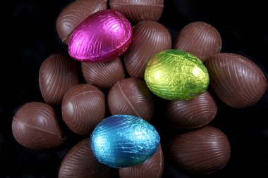 Yığın folyo sarılı ve unwrapped çikolata Paskalya yumurtaları içinde pembe, mavi ve kireç yeşil, siyah bir arka plan karşı.
