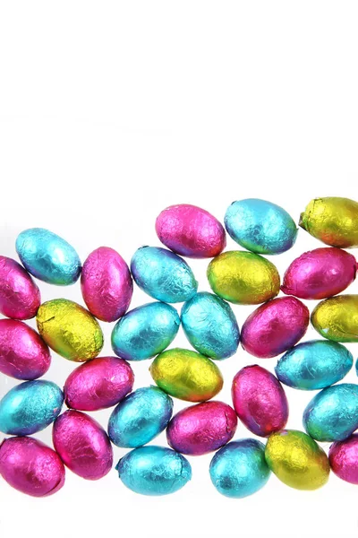 Pilha de papel alumínio embrulhado ovos de Páscoa de chocolate em rosa, azul e verde limão com um fundo branco . Fotos De Bancos De Imagens