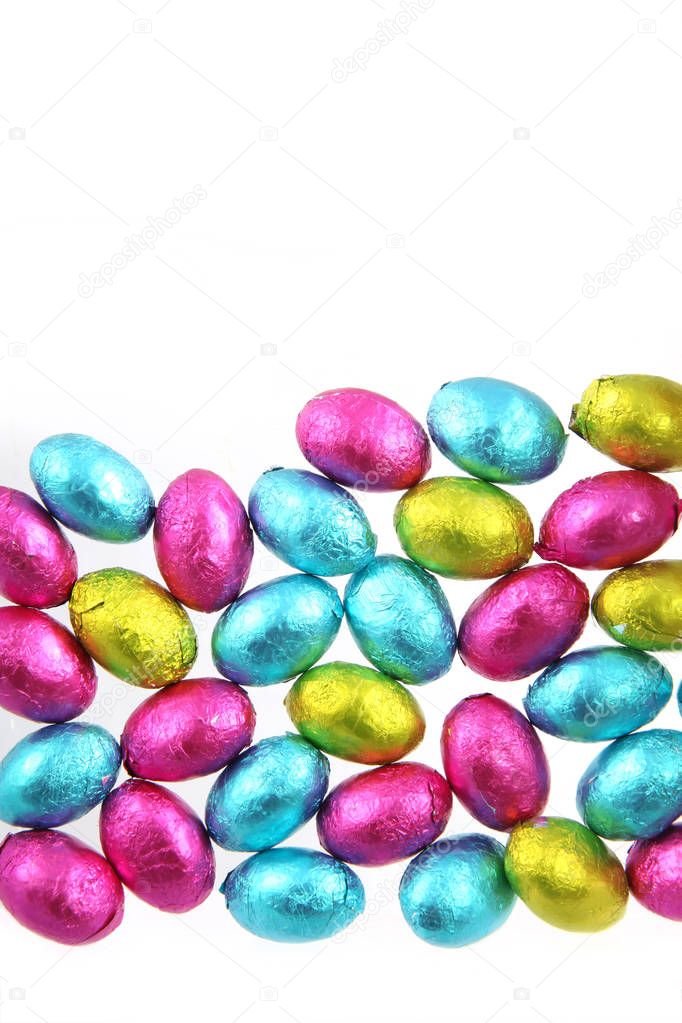 Pile of foil wrapped chocolate easter eggs in pink, blue & lime green with a white background.
