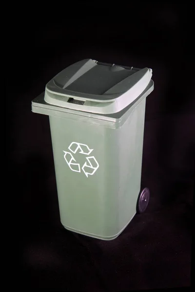 Green recycle rubbish or garbage bin with the recycle symbol on a black background.