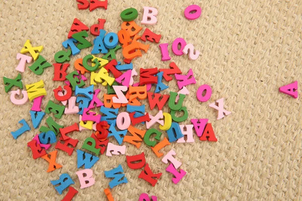 Multi coloured wooden letters in red, green, blue, pink & yellow. The letters are a childrens toy & are scattered on the floor. They are a fun way to learn spelling.