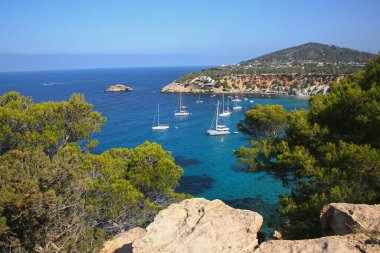 Ibiza 'nın güney kıyısından, körfeze demir atmış tekneleri gösteren görüntü. Uçurumları ve turkuaz suları olan güzel bir manzara. Balerik Adaları, İspanya.