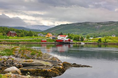 Su kenarında güzel bir manzara, arka planda bir köy ve kilise & dağları, Saltstraumen, Bodo Belediyesi, Nordland İlçesi, Norveç. 
