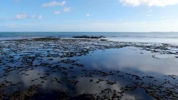 Luftaufnahme über Felsen und Ozean mit der Reflexion des Himmels auf dem Wasser. — Stockvideo