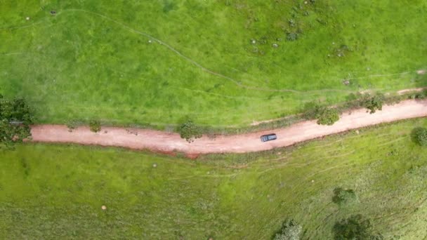 Aerial view of car driving throuh a small dirt road in the middle of green tropical valley. — Stock Video