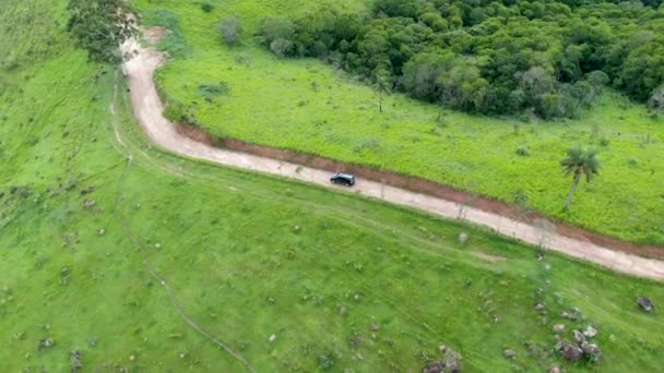 Aerial view of car driving throuh a small dirt road in the middle of green tropical valley. — Stock Video