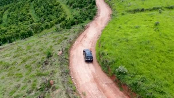 緑の熱帯の谷の真ん中に小さな未舗装の道路を車の運転の空中ビュー. — ストック動画