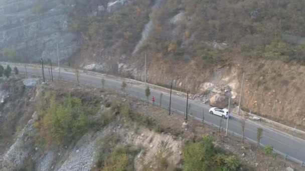 Aerial view of white car driving on a small asphalt road in a dry mountain — Stock Video