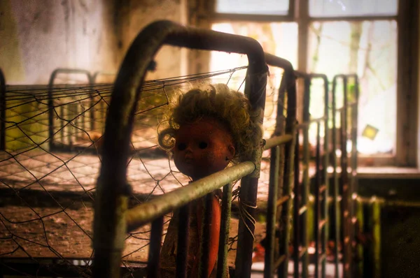 Çernobil bölgesindeki terk edilmiş anaokulunun içinde. Önünde eski bir bebek, arkasında parlak bir pencere olan yataklar..