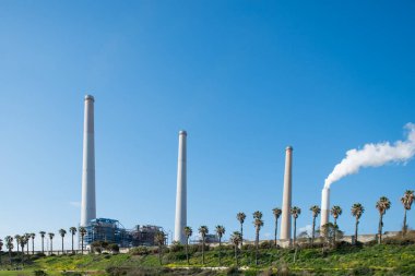 Mavi gökyüzüne karşı elektrik santrali bacalarından duman yükseliyor. Hadera, İsrail enerji santrali.