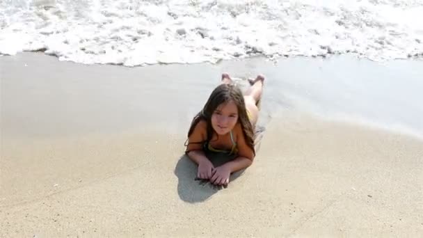 Niña tendida en la arena, las olas del mar salpicando en su cuerpo — Vídeos de Stock