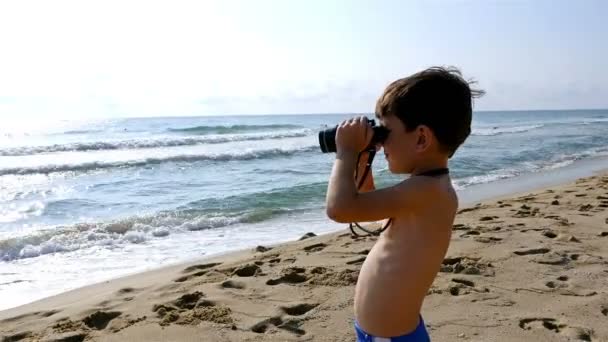 Little boy in swimsuit uses binoculars to explore the sea — Stock Video