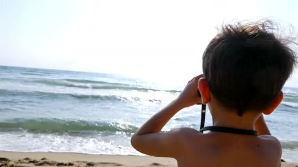 Niño en traje de baño utiliza prismáticos para explorar el mar — Vídeos de Stock