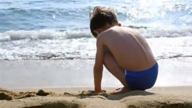 Denizin kenarında kumla oynayan mayo küçük çocuk