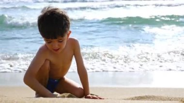 Denizin kenarında kumla oynayan mayo küçük çocuk