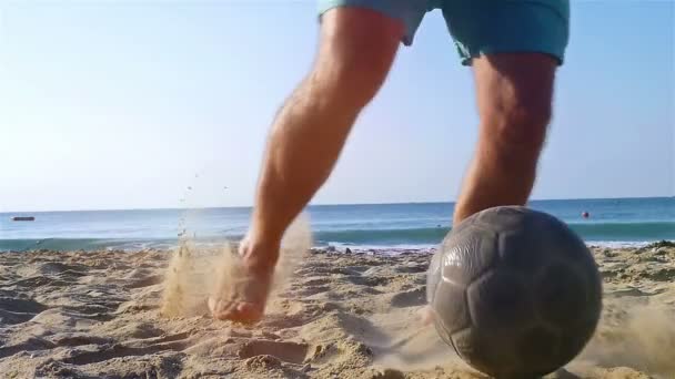 Pies masculinos pateando pelota de fútbol en la playa del mar, cámara lenta — Vídeos de Stock