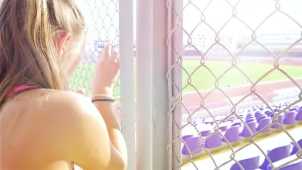 Tiener meisje atleet is triest boos ongelukkig teleurgesteld wire-netting houden in een stadion — Stockvideo