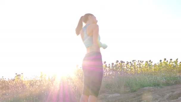 Tracking camera of woman girl with headphones running jogging in sunflower field — Stock video