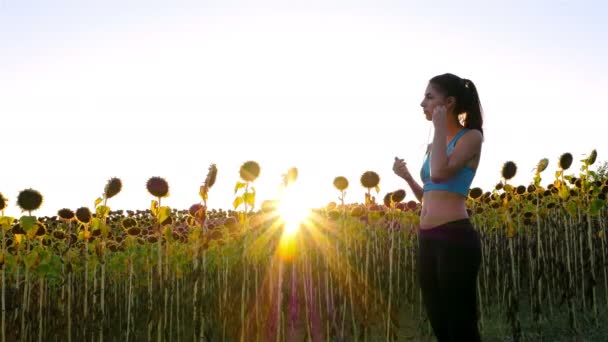 Tracking camera of woman girl with headphones running jogging in sunflower field — Stock Video