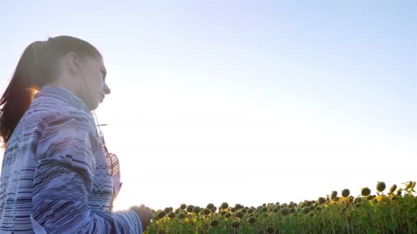 Tracking camera of woman girl with headphones running jogging in sunflower field — Stock video