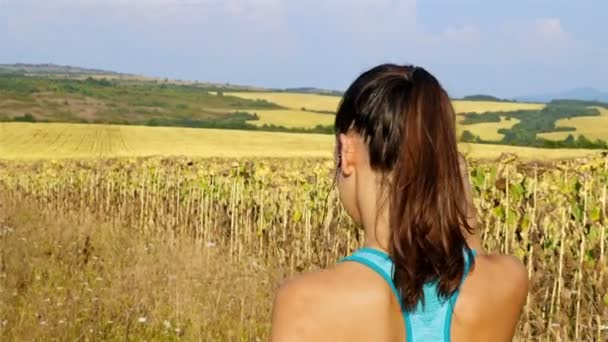 Tracking camera of woman girl with headphones running jogging in sunflower field — ストック動画