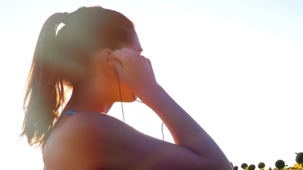 Cámara de seguimiento de mujer chica con auriculares corriendo corriendo en el campo de girasol, cámara lenta — Vídeos de Stock