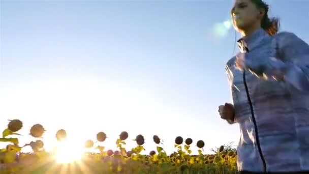 Отслеживание камеры женщина девушка с наушниками работает бег трусцой на подсолнечном поле, замедленная съемка — стоковое видео