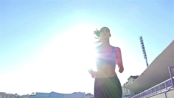 Отслеживающая камера бегущей по треку спортсменки девушки бегущей на стадионе, низкий угол, солнечная вспышка, замедленная съемка — стоковое видео