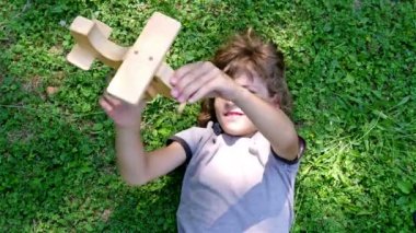 Yeşil çimenlerin üzerinde üstten görünüm yalan ahşap oyuncak uçak ile oynayan çocuk