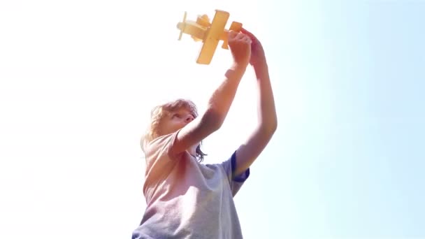 Low angle shot of a boy playing with wooden toy airplane against blue sky — Stock video