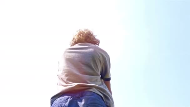 Low angle shot of a boy playing with wooden toy airplane against blue sky — Stockvideo