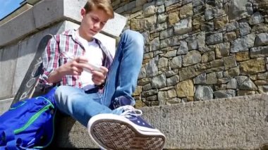 Kaykay ve sırt çantası yazılı sms, mesaj smartphone cep telefonu ile merdivenlerde oturan bir genç çocuk