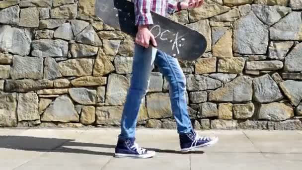 Мальчик-подросток со скейтбордом ходит с помощью смартфона в городе — стоковое видео