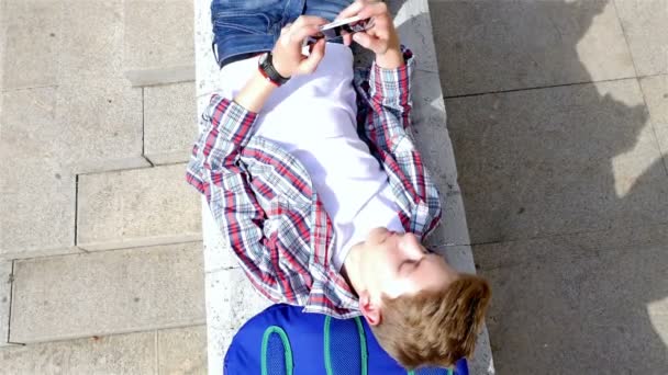 Nastolatek chłopiec pisanie sms, SMS-y na smartphone, leżącego w miasto, widok z góry — Wideo stockowe