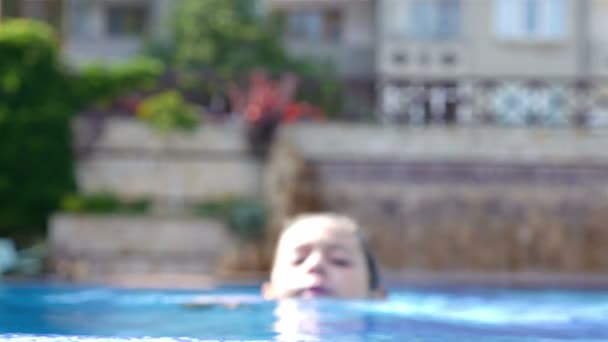 Портрет милой маленькой девочки, плывущей к краю бассейна и улыбающейся — стоковое видео