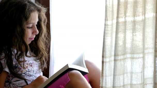 Petite fille mignonne assise sur le rebord de la fenêtre d'une vieille maison, lisant un livre à son jouet d'ours — Video