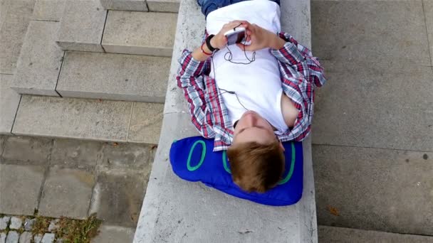 Adolescente menino escrevendo sms, mensagens de texto no smartphone deitado na cidade, vista superior — Vídeo de Stock