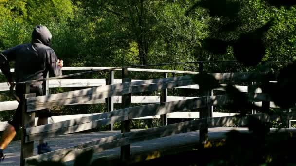 Homme à capuchon courant sur un pont en bois dans le bois 