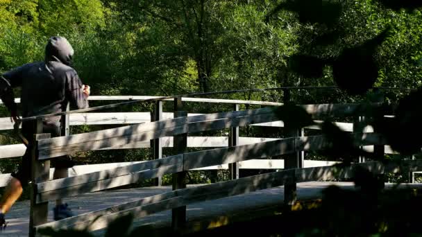 Homme à capuchon courant sur un pont en bois dans le bois — Video