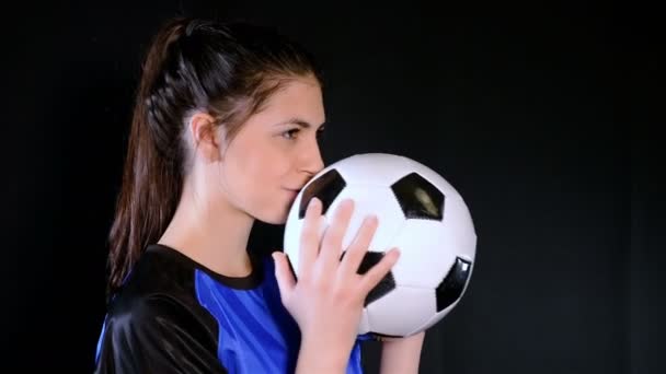 Female soccer player kissing the ball before kicking it on black background — Stock Video