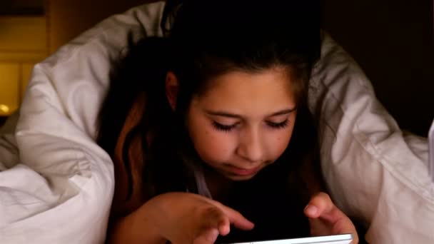 可爱的小女孩，在一个黑暗的房间里使用 tablet pc 在毯子下面。胜利的手势. — 图库视频影像