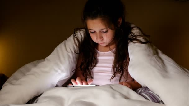 Menina bonito usando tablet pc sob cobertor em um quarto escuro. Gesto vencedor . — Vídeo de Stock