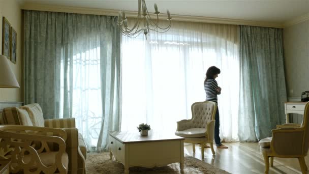 Расстроенная женщина ходит туда-сюда вдоль окна уютной квартиры — стоковое видео