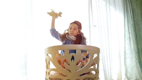 Bambina con cappello da pilota che gioca a braccia aperte come un aeroplano in un accogliente appartamento, orsacchiotto in grembo, 4k — Video Stock