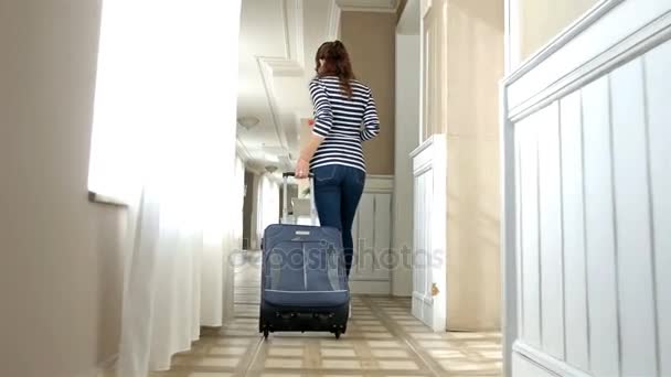 Caucasian woman walking in a long light corridor of a hotel with a suitcase entering the room — Stock Video