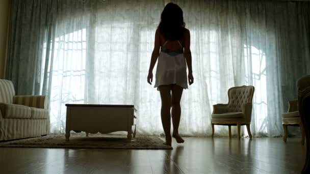 Kvinna i ett nattlinne avslöja gardiner i rummet på morgonen — Stockvideo