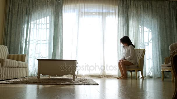 Расстроенная женщина в рубашке ходит туда-сюда вдоль окна уютной квартиры — стоковое видео